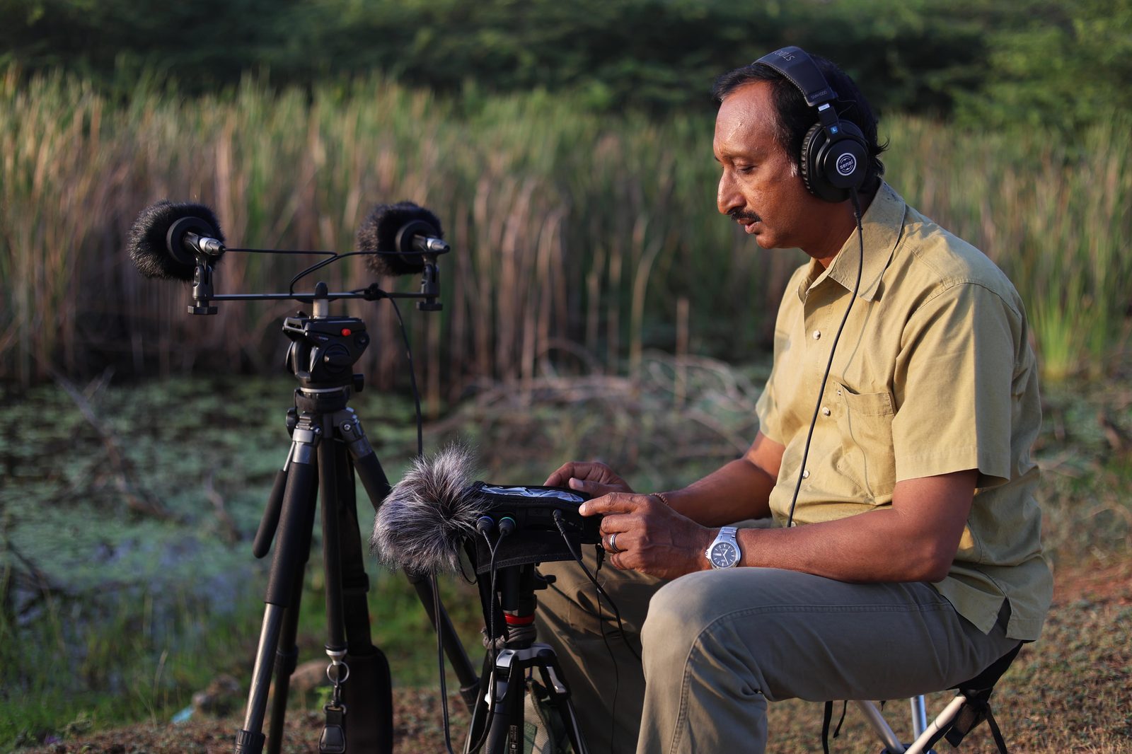 Deepal Warakagoda recording natural sound in the field, wearing headphones beside a stereo microphone rig and a portable recorder.